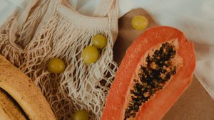 Close-up of fresh papaya, bananas, and grapes in a mesh bag on a wooden board.